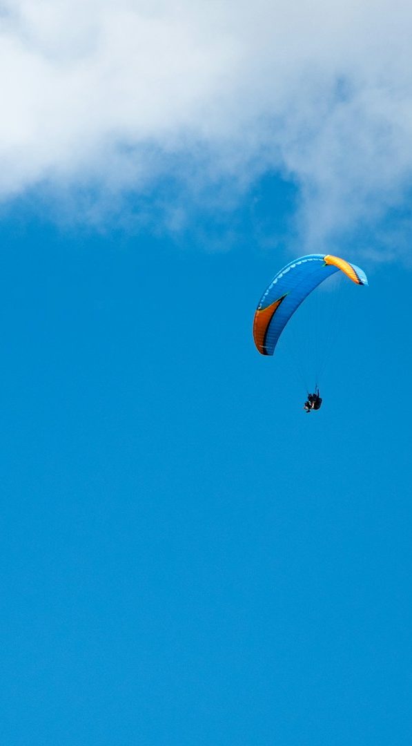 parapente Un parapente coloré plane dans un ciel bleu avec quelques nuages.