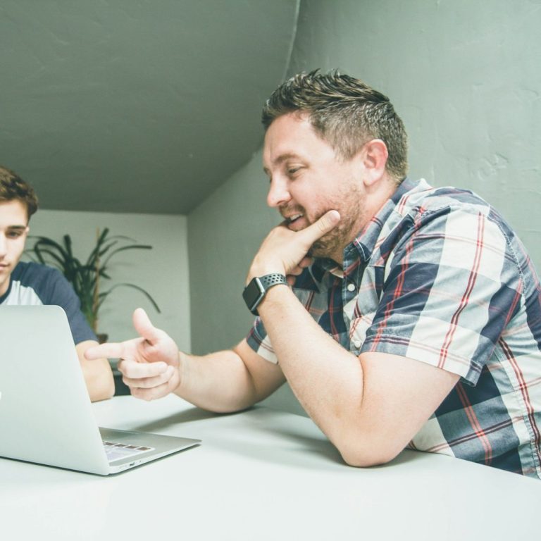 tuteur ou maitre d'apprentissage Deux hommes (un jeune et un moins jeune) discutent devant un ordinateur portable dans un cadre intérieur moderne.