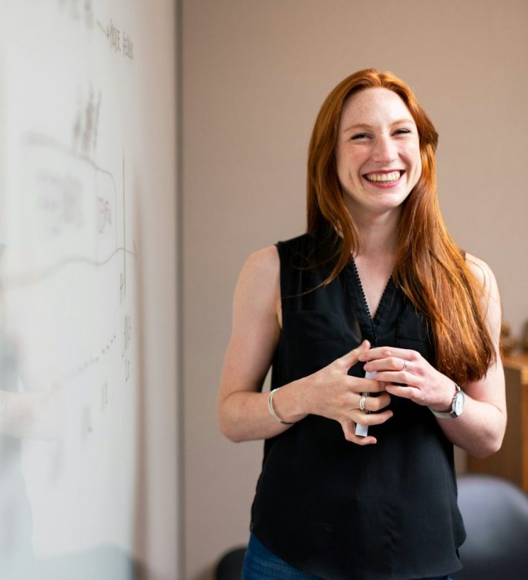 formatrice Femme souriante présentant des informations devant un tableau, en conversant avec une autre personne.